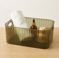 Green rectangular basket with a white towel, brown bottle, and wooden brush on a wooden surface.
